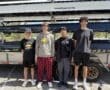 Four young rowers pose together by their boat trailer, showcasing their team spirit on a sunny day.