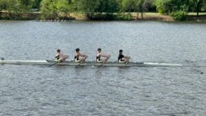 Four rowers in a boat compete on a serene river, showcasing teamwork and athleticism on a sunny day.