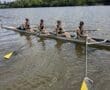 Four rowers in matching uniforms enjoying a sunny day on the water as they practice rowing on a calm river.