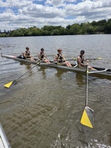 Four rowers in matching uniforms enjoying a sunny day on the water as they practice rowing on a calm river.