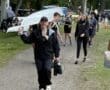 A group of rowers carrying a boat and gear along a path in a green park, smiling and enjoying the team spirit.
