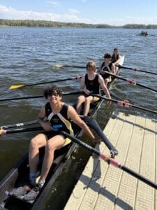 Rowing team preparing to launch on a sunny day, showcasing teamwork on the water with their oars ready.