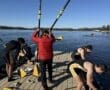 Rowers preparing their boats on a dock by the water on a clear day, with a coach guiding the team.