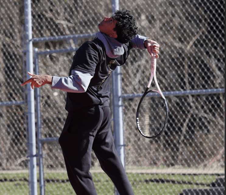 Young athlete serving a tennis ball on a court, showcasing focus and determination in an outdoor setting.