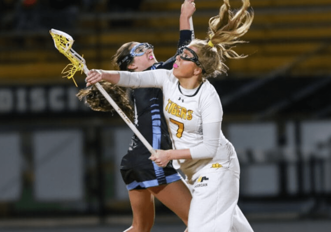 Girls' lacrosse players compete fiercely, showcasing athleticism and teamwork in an intense match under the lights.