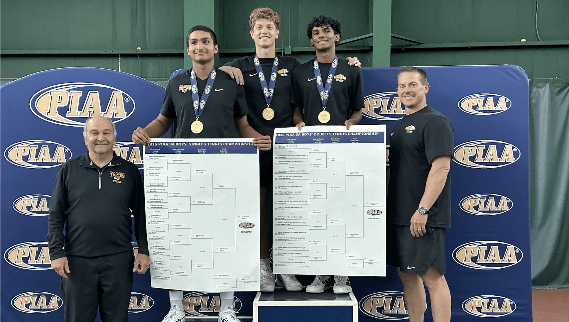 PIAA tennis champions celebrate victory, holding brackets for singles and doubles championships, with coaches.