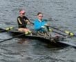 Two women rowing together in a boat on a calm lake, enjoying a sunny day outdoors.