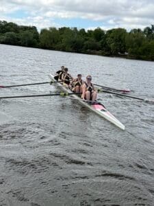 A rowing team in a sleek boat competes on a river under a partly cloudy sky, showcasing teamwork and athleticism.