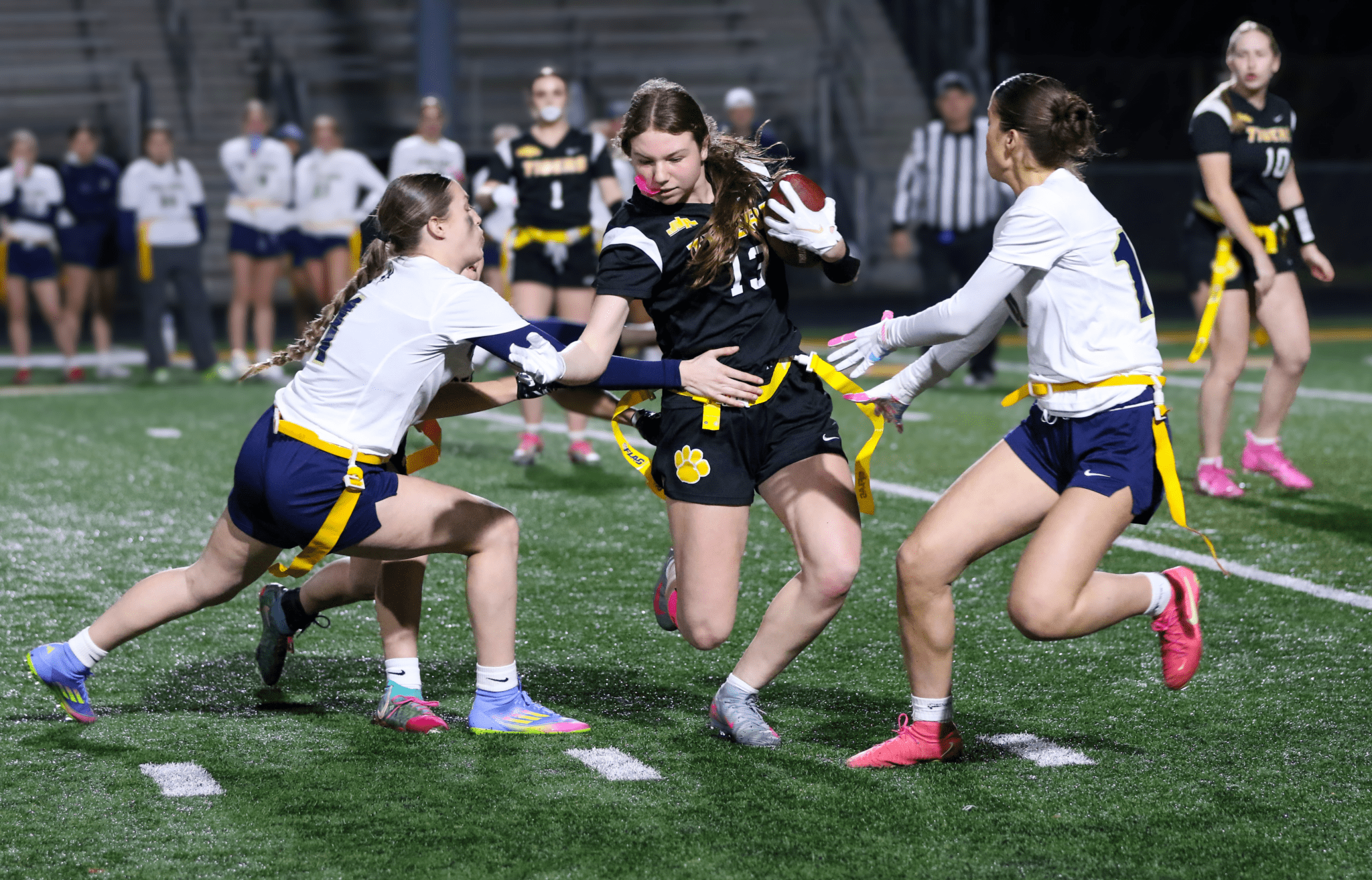 Action shot of female players in a flag football game, one dodging tackles while carrying the ball on a field.