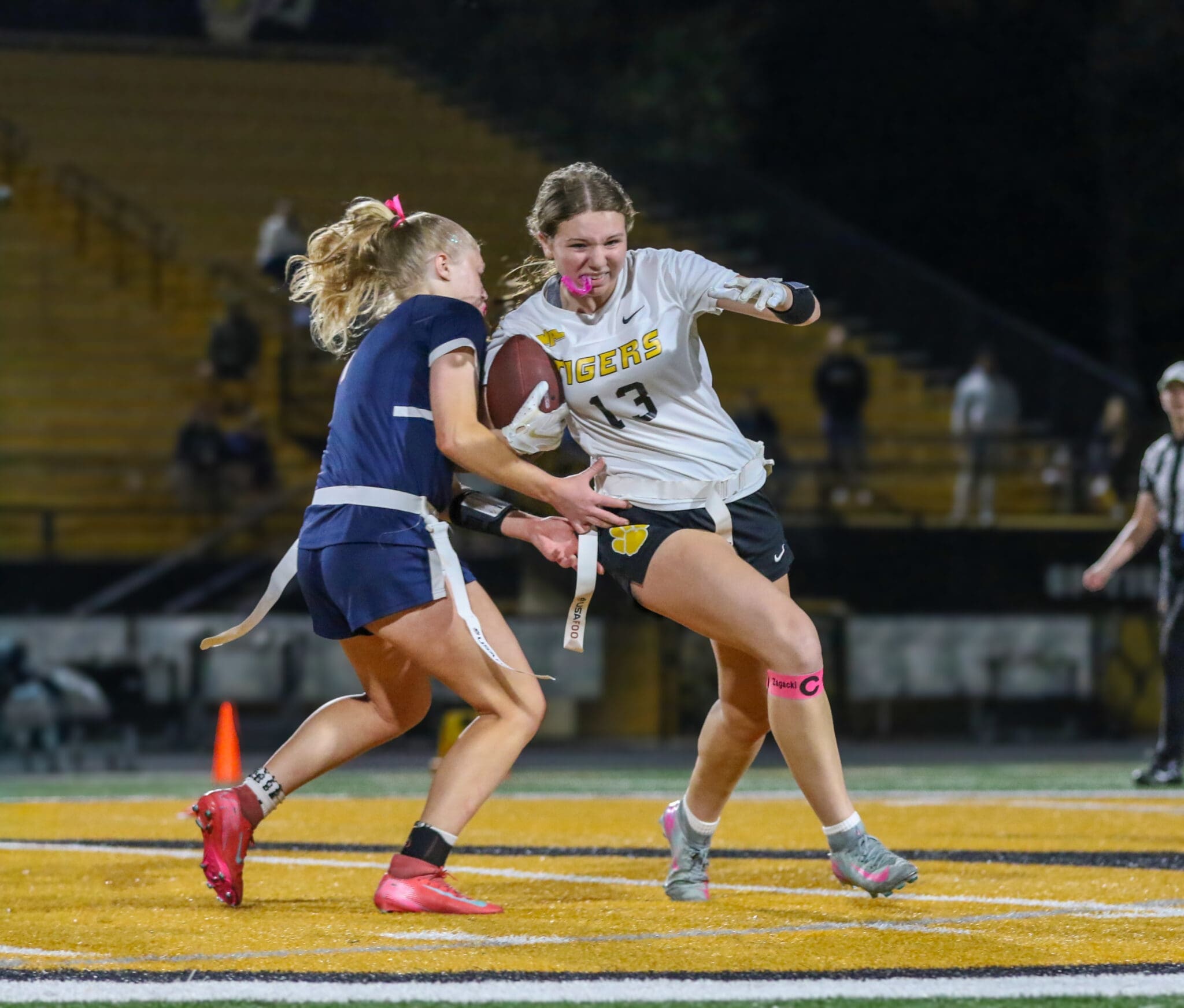 Flag football action shot: A player in a white jersey dodges an opponent in a blue uniform during a competitive game.