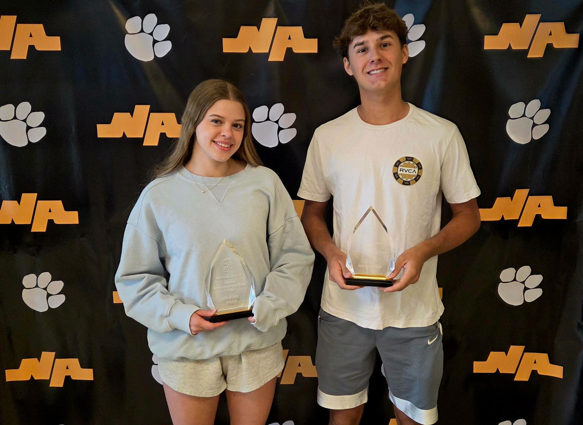 Two students proudly holding their awards in front of a North Atlanta High School backdrop featuring paw prints.
