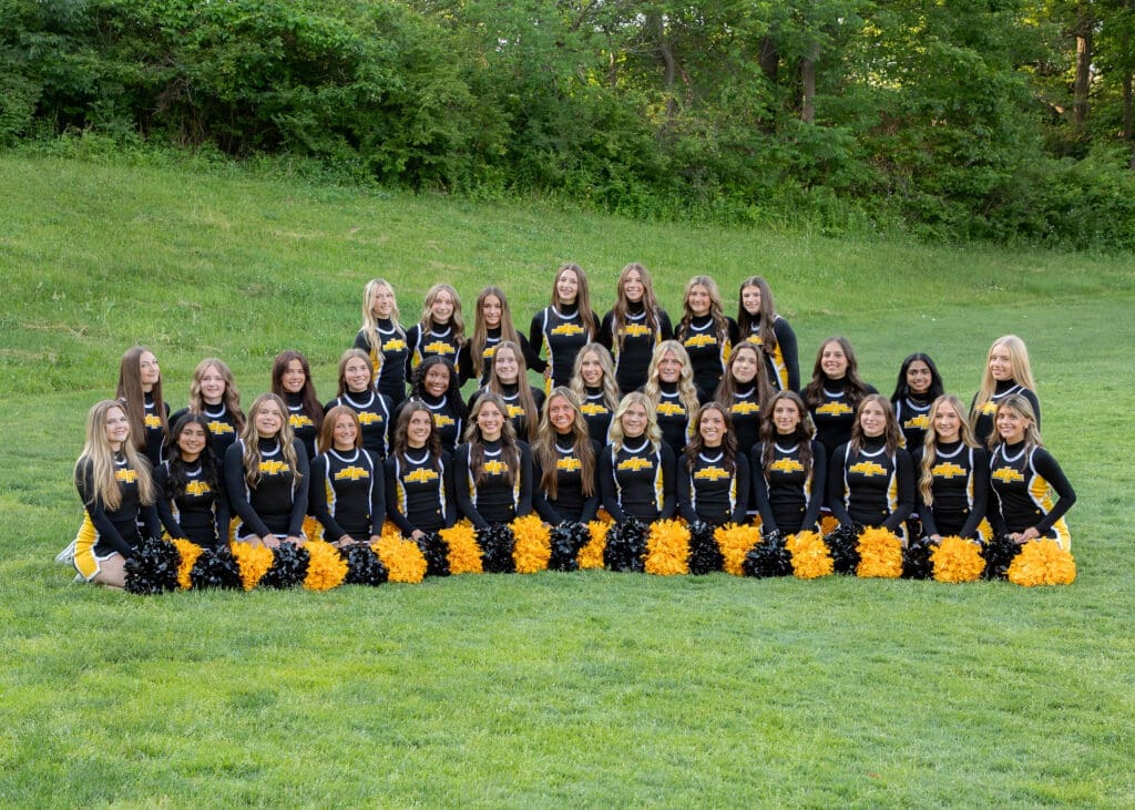 Cheerleading squad photo featuring 30 girls in black and yellow uniforms, posing with pom-poms on a grassy field.
