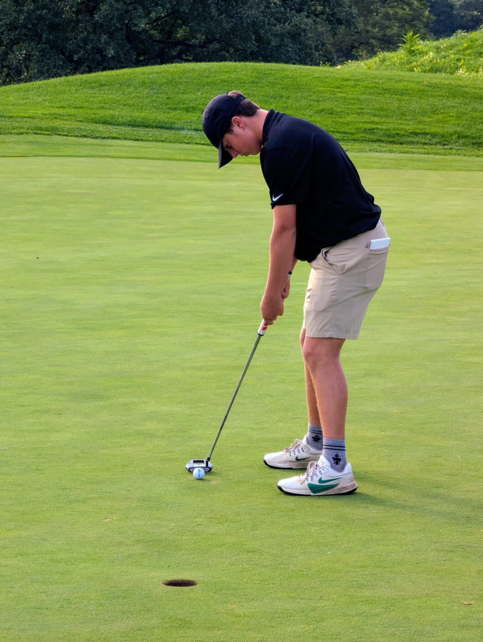 A young golfer focusing intently on putting a golf ball on a well-maintained green.