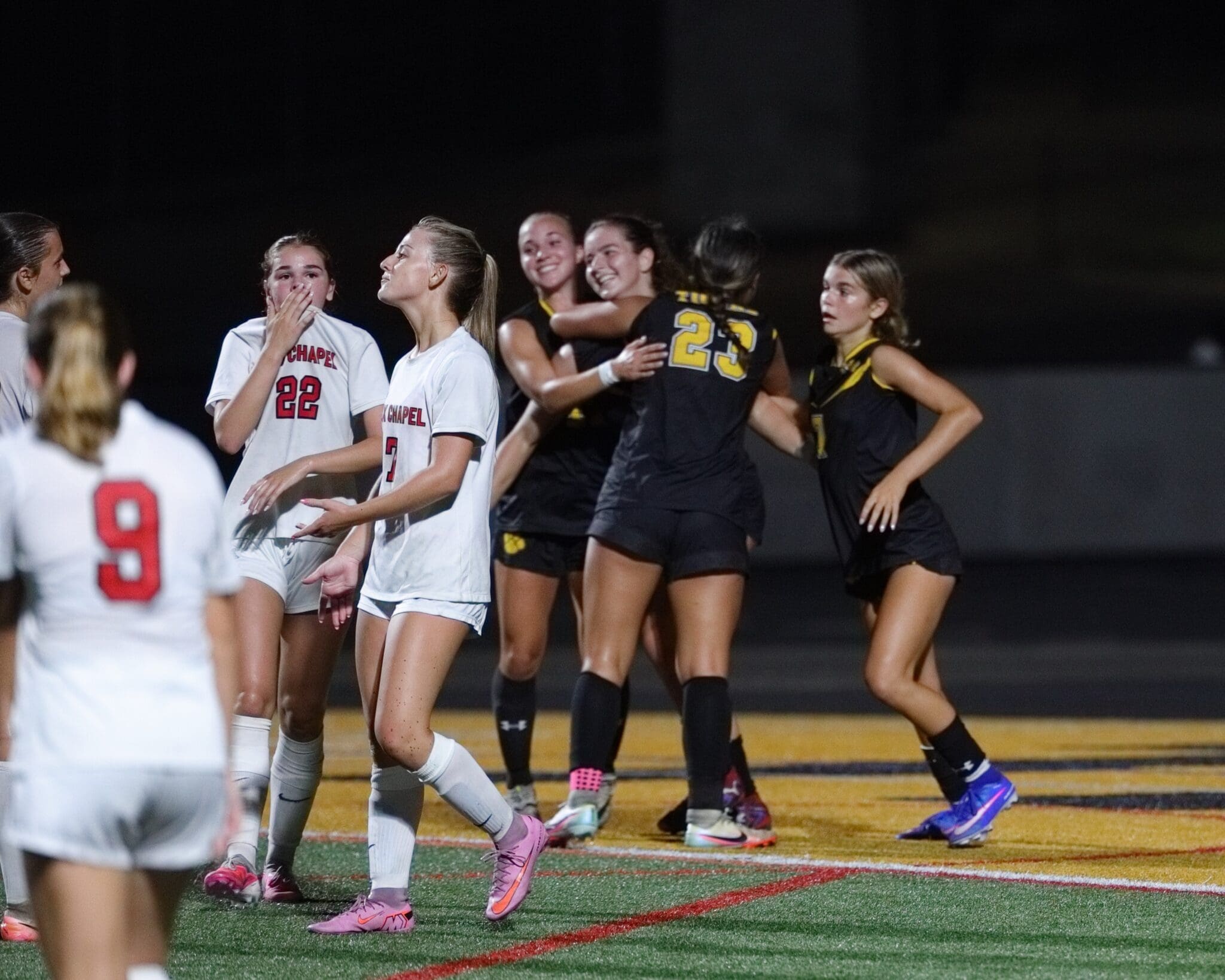 High school girls' soccer players celebrate a goal under the stadium lights during a thrilling match.