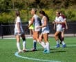 Four female soccer players celebrate on the field during a match, showcasing teamwork and sportsmanship in action.