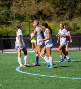 Four female soccer players celebrate on the field during a match, showcasing teamwork and sportsmanship in action.