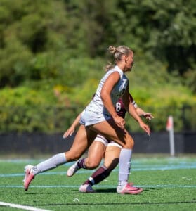 A female soccer player sprinting on the field during a match, showcasing athleticism and teamwork in action.