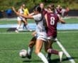 Two female soccer players compete for the ball on a green turf field during a heated match.
