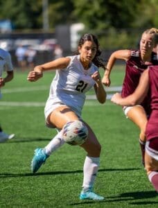 Female soccer player in action, skillfully kicking a ball during a competitive match on a sunny day.