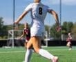 Female soccer player wearing jersey number 8 dribbles the ball on a sunny field during a match.