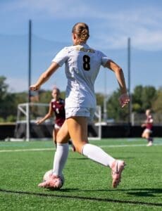 Female soccer player wearing jersey number 8 dribbles the ball on a sunny field during a match.