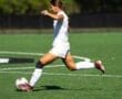 Young female soccer player dribbling a ball on an artificial turf field, showcasing athleticism and focus.