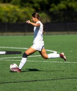 Young female soccer player dribbling a ball on an artificial turf field, showcasing athleticism and focus.