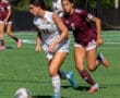 Two female soccer players compete for the ball on a sunny field, showcasing athleticism and sportsmanship during a match.