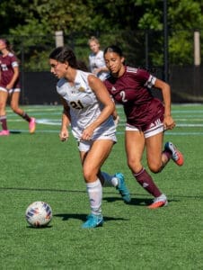 Two female soccer players compete for the ball on a sunny field, showcasing athleticism and sportsmanship during a match.