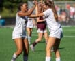 Two female soccer players celebrate with high-fives on the field, showcasing teamwork and sportsmanship on a sunny day.