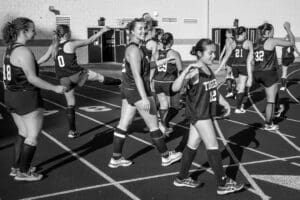 A group of female athletes in black jerseys warming up on a track, showcasing teamwork and camaraderie.