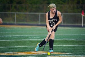 Field hockey player in action on a turf field, wearing a black jersey with the number 20, focused on the ball.