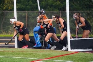 Field hockey team preparing for play, showcasing athletes in uniforms and a goalie in position at the goal.