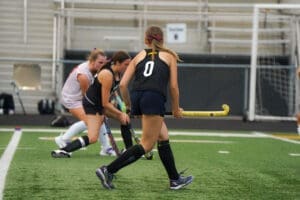 Field hockey players practice on a turf field, focusing on teamwork and skills during a training session.