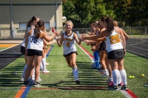 Field hockey players celebrate teammate as she runs through a spirit line, showcasing team spirit and camaraderie.