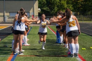 High school field hockey players celebrate a teammate with high-fives during a game day introduction on the field.