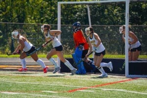 Field hockey players in action during a game, showcasing teamwork and athleticism in front of the goal.