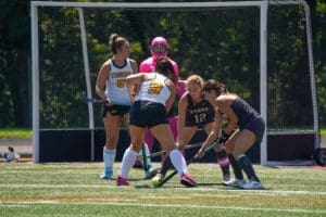 Field hockey players compete for the ball during a match, showcasing teamwork and strategy on the turf.