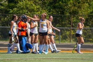 Field hockey team celebrating and strategizing during a game, showcasing teamwork and athletic spirit on a sunny day.