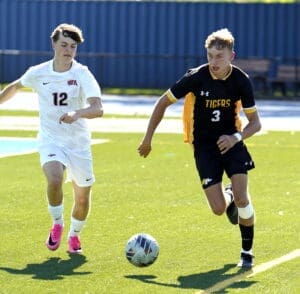 Two high school soccer players compete for the ball on a sunny, green field during an intense match.