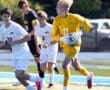 High school soccer players in action; goalie's catching the ball, while teammates sprint in competitive match.