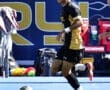 Player in a black and gold soccer uniform dribbling the ball during a game, focused on the field ahead.