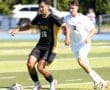 High school soccer players in action, one in a black jersey dribbling the ball, another close behind in white.