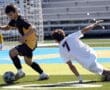 Action shot of a soccer player dribbling the ball while another player attempts to tackle on a sunny field.