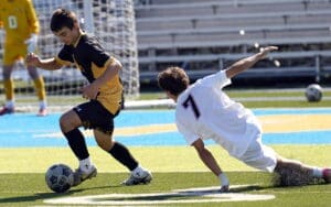 Action shot of a soccer player dribbling the ball while another player attempts to tackle on a sunny field.