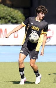 High school soccer player in action, wearing a black and yellow Tigers jersey, juggling a soccer ball on the field.