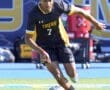 Young soccer player in a black Tigers jersey dribbling the ball during an intense game on a sunny field.