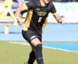Soccer player in black and gold uniform dribbling the ball on a sunny field, focused and in motion.