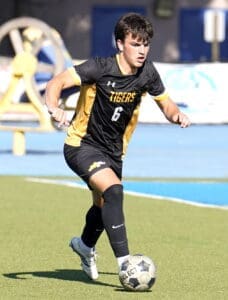 Soccer player in black and gold uniform dribbling the ball on a sunny field, focused and in motion.