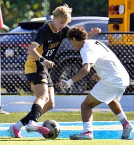Two soccer players in a competitive match, one in black and yellow, the other in white, attempting to gain control of the ball.